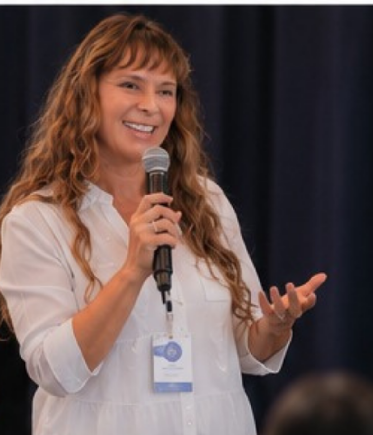Débora Dubay, especialista em Gestão Emocional e Alta Performance, sorrindo de forma empática enquanto ministra palestra com um microfone em um evento corporativo.